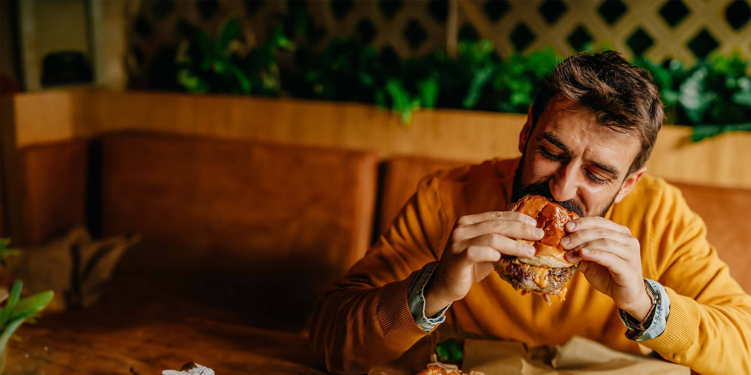 Ein Mann beißt unvorteilhaft in einen Hamburger. 